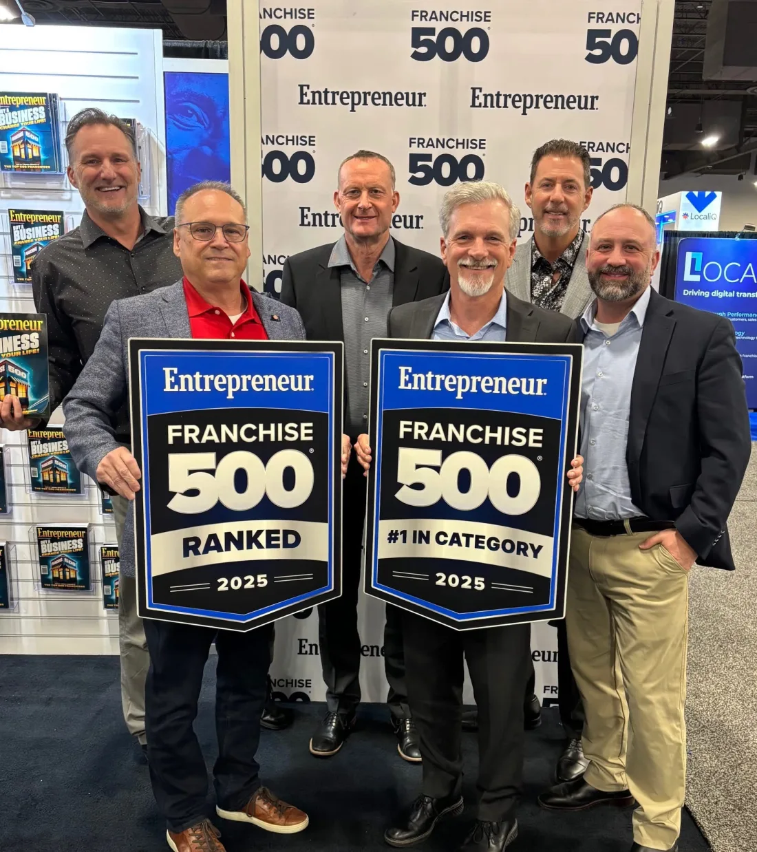 Six men at the Entrepreneur Franchise 500 backdrop holding two 2025 plaques