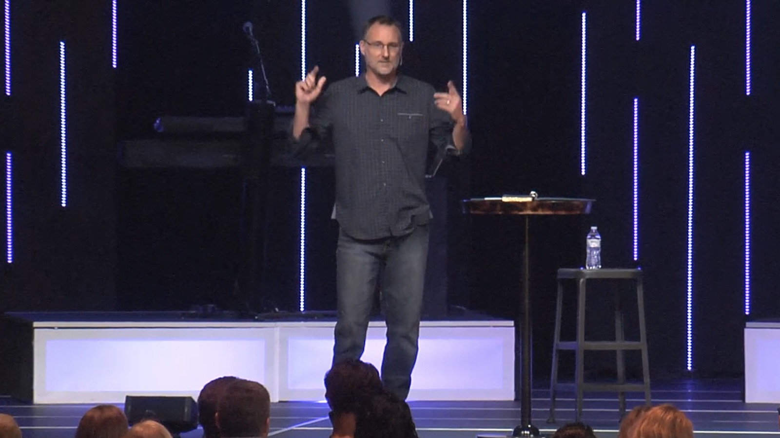 Mike Millett on stage with both hands raised, engaging a live audience