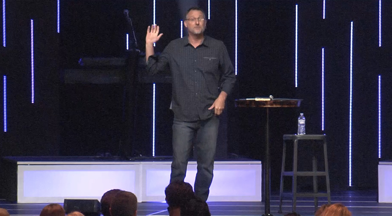 Mike Millett presenting on a large conference stage with dramatic vertical LED light strips